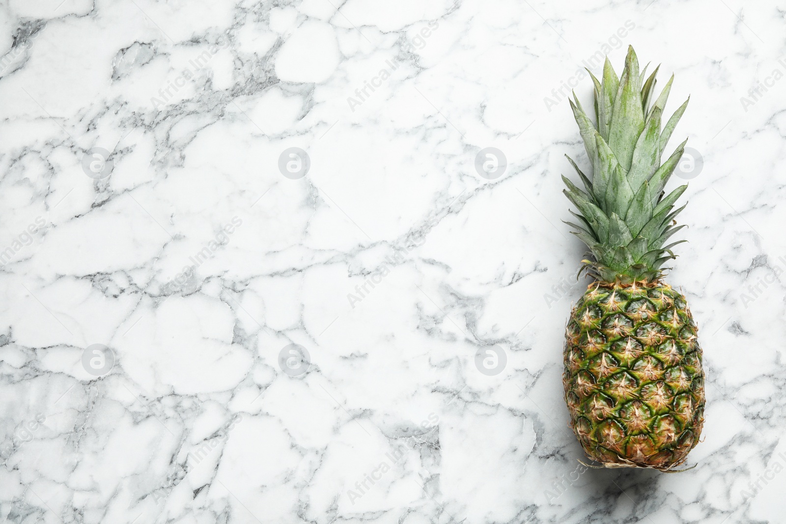 Photo of Fresh whole pineapple on white marble background, top view. Space for text