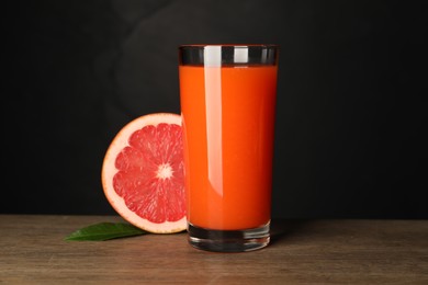 Photo of Tasty grapefruit juice in glass, leaf and fresh fruit on wooden table against black background