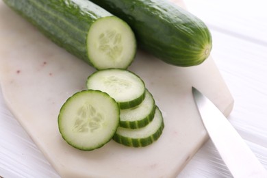 Photo of Cucumbers, knife and marble cutting board on white wooden table, closeup