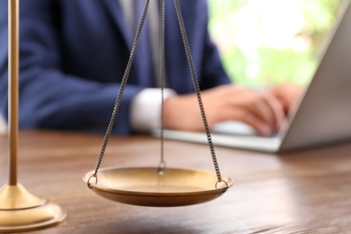 Scales of justice and blurred lawyer working with laptop on background