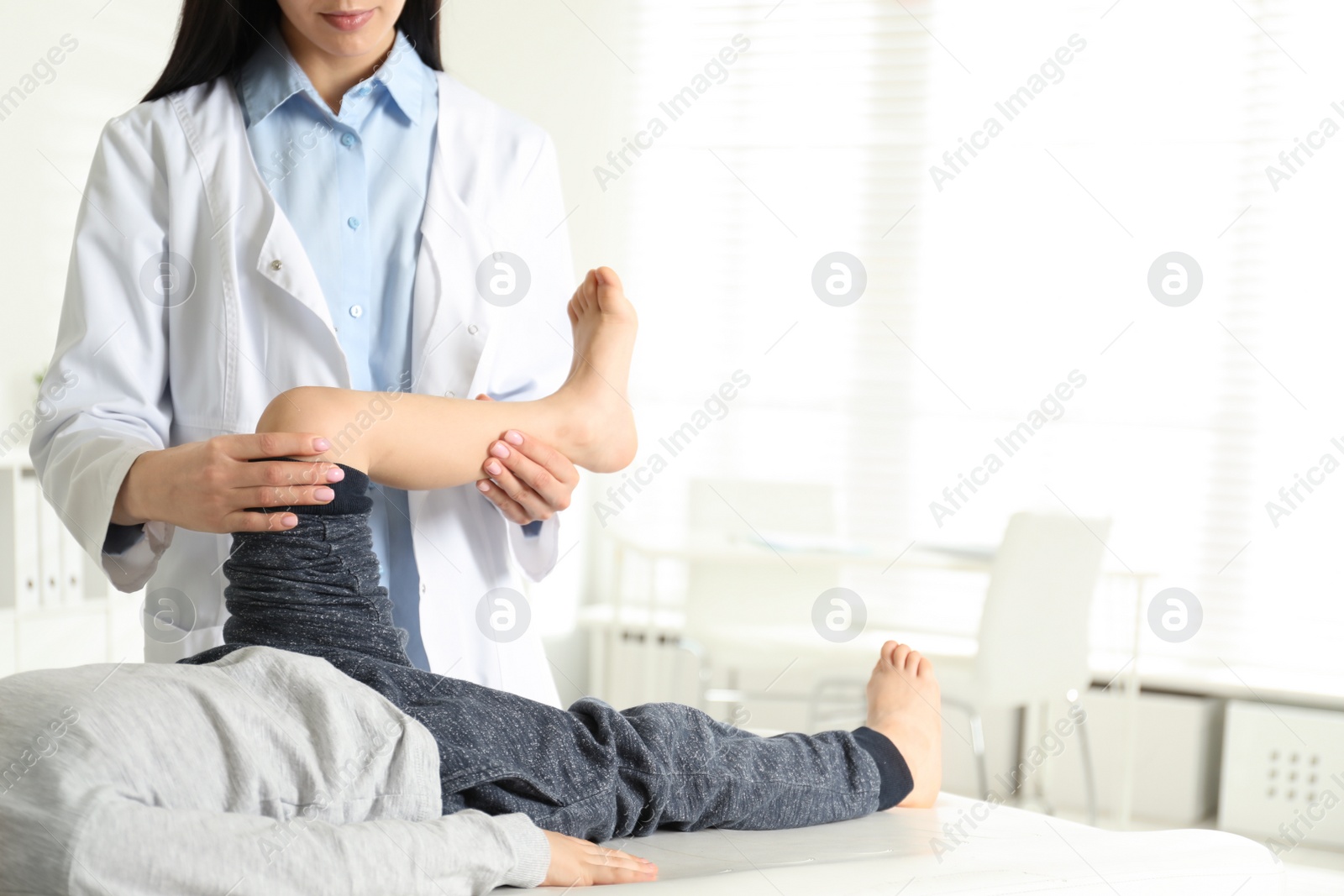 Photo of Professional orthopedist examining little patient's leg in clinic. Space for text