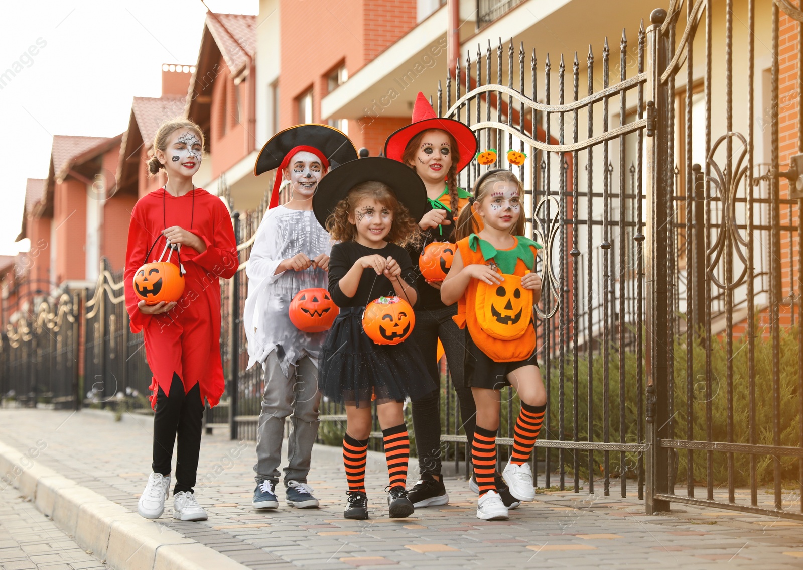 Photo of Cute little kids wearing Halloween costumes going trick-or-treating outdoors