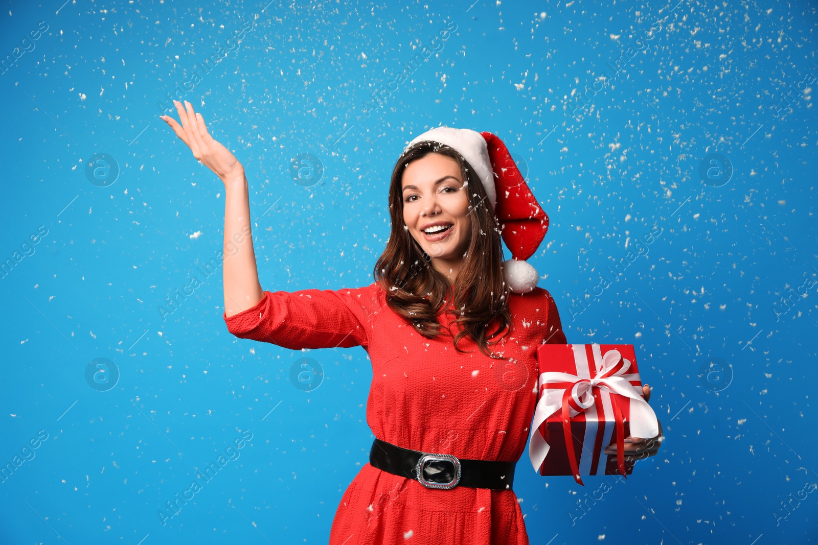 Photo of Beautiful woman wearing Santa hat with Christmas gift on light blue background