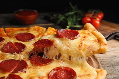 Photo of Taking slice of tasty pepperoni pizza on wooden table, closeup