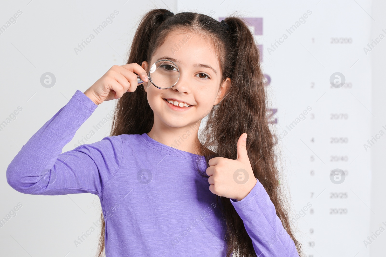 Photo of Little girl with magnifier visiting children's doctor. Eye examination