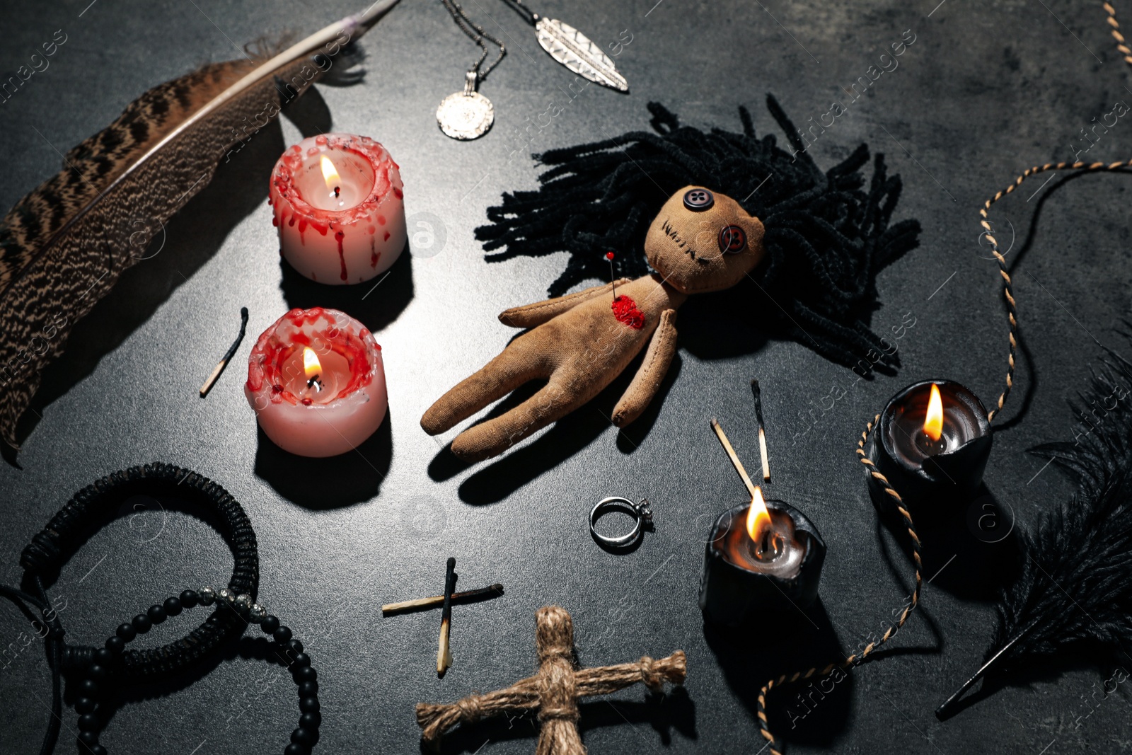 Photo of Female voodoo doll with pin in heart and ceremonial items on grey table