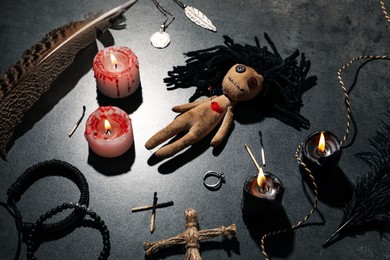 Photo of Female voodoo doll with pin in heart and ceremonial items on grey table