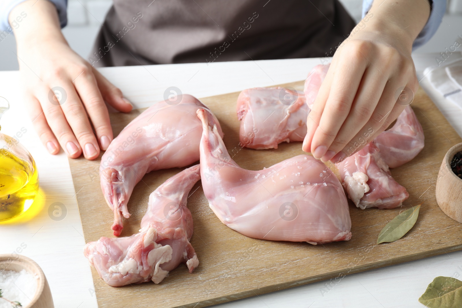 Photo of Woman putting salt onto raw rabbit meat at white wooden table, closeup