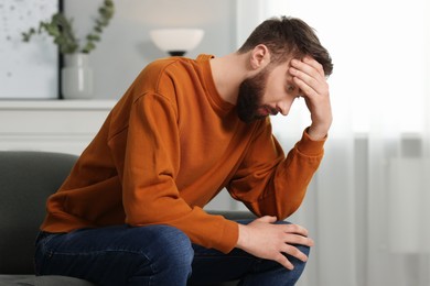 Photo of Overwhelmed man sitting on sofa at home