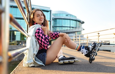 Photo of Beautiful young woman with roller skates sitting outdoors