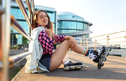 Beautiful young woman with roller skates sitting outdoors