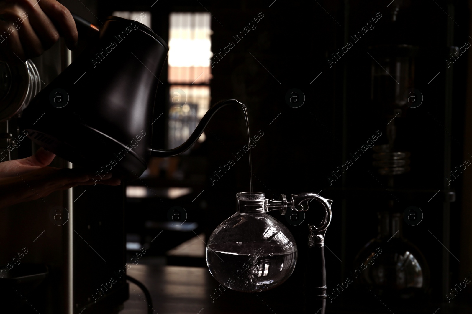Photo of Barista pouring water into vacuum coffee maker at table in cafe, closeup