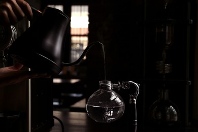 Photo of Barista pouring water into vacuum coffee maker at table in cafe, closeup