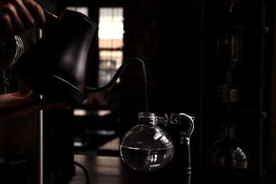 Barista pouring water into vacuum coffee maker at table in cafe, closeup