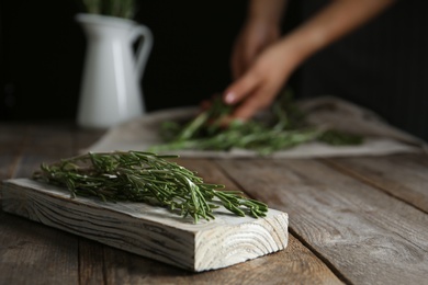 Photo of Wooden board with fresh green rosemary and woman on background. Aromatic herbs