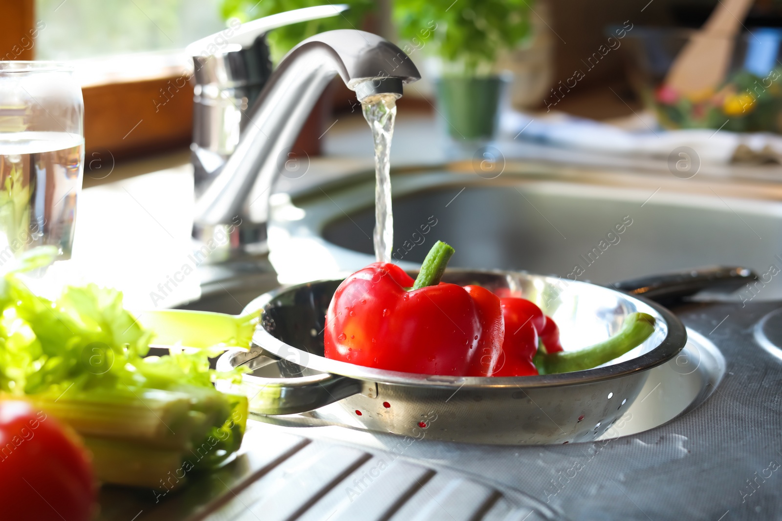 Photo of Washing fresh bell peppers in colander under kitchen tap