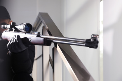 Photo of Hired professional killer with sniper rifle indoors, closeup