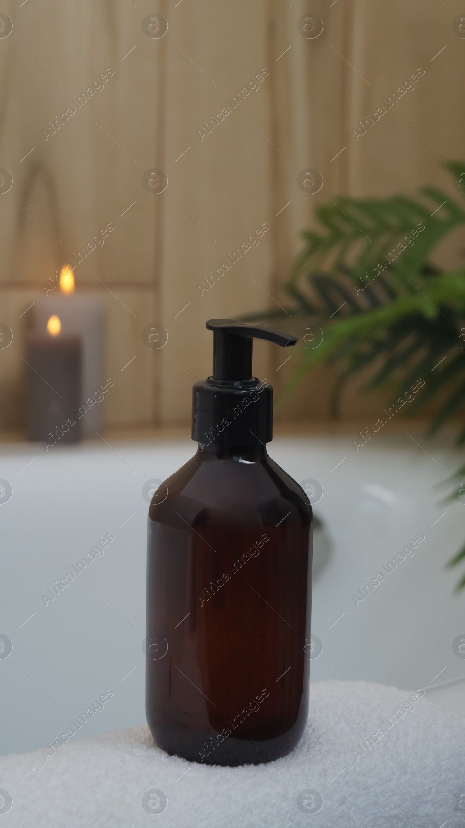 Photo of Black bottle of bubble bath and candles on tub indoors
