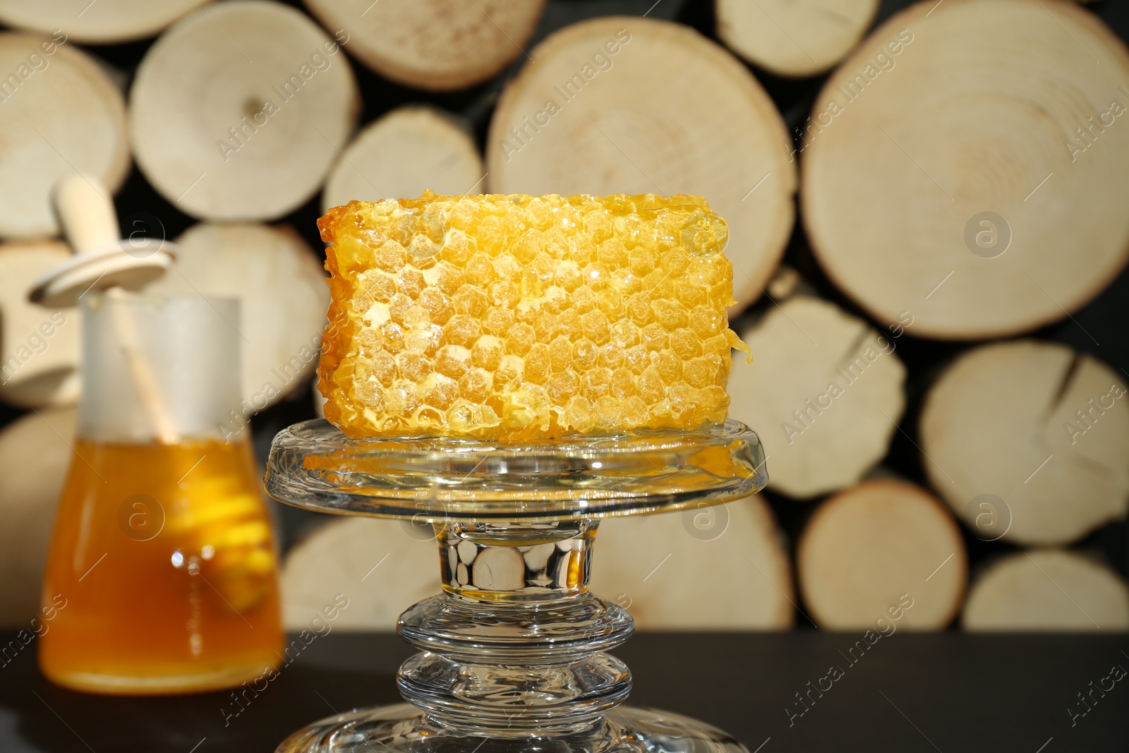 Photo of Glass stand with natural honeycomb and honey on black table, selective focus. Space for text