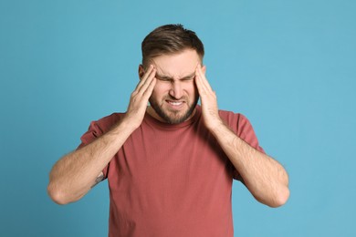 Man suffering from migraine on light blue background