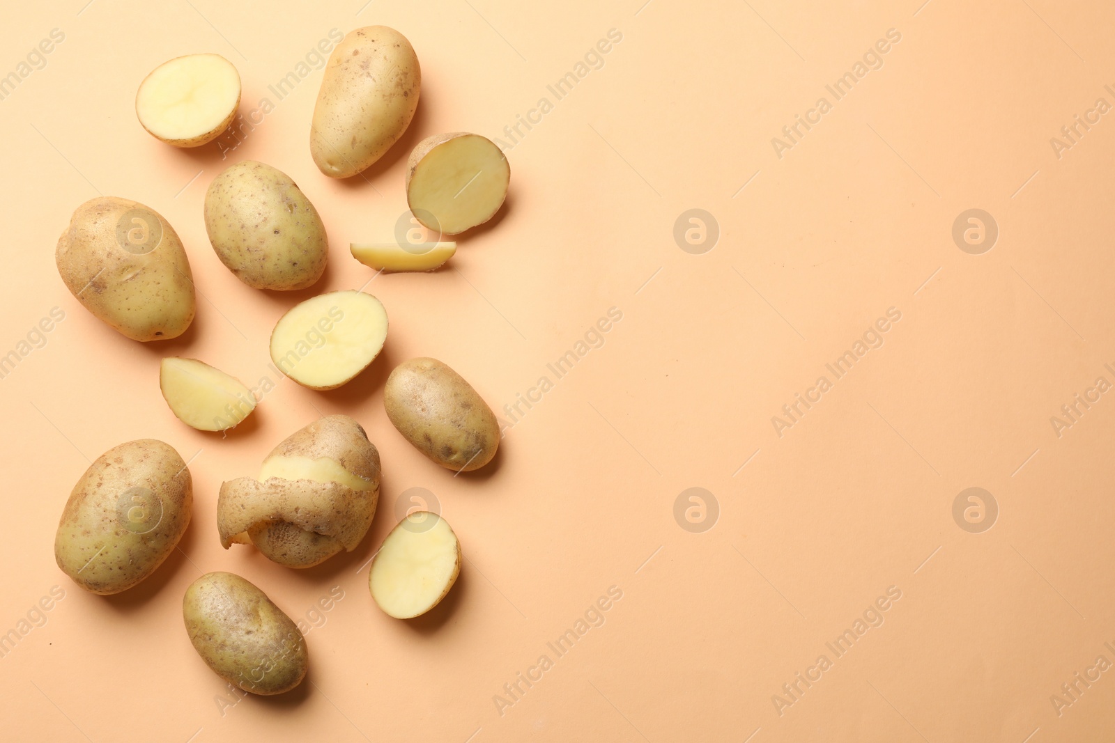 Photo of Fresh raw potatoes on pale orange background, flat lay. Space for text