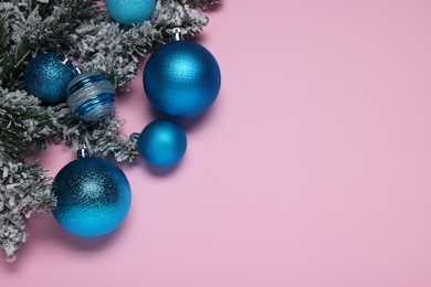 Shiny blue Christmas balls and fir tree branches with snow on pink background, flat lay. Space for text