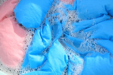 Photo of Colorful clothes in suds, top view. Hand washing laundry