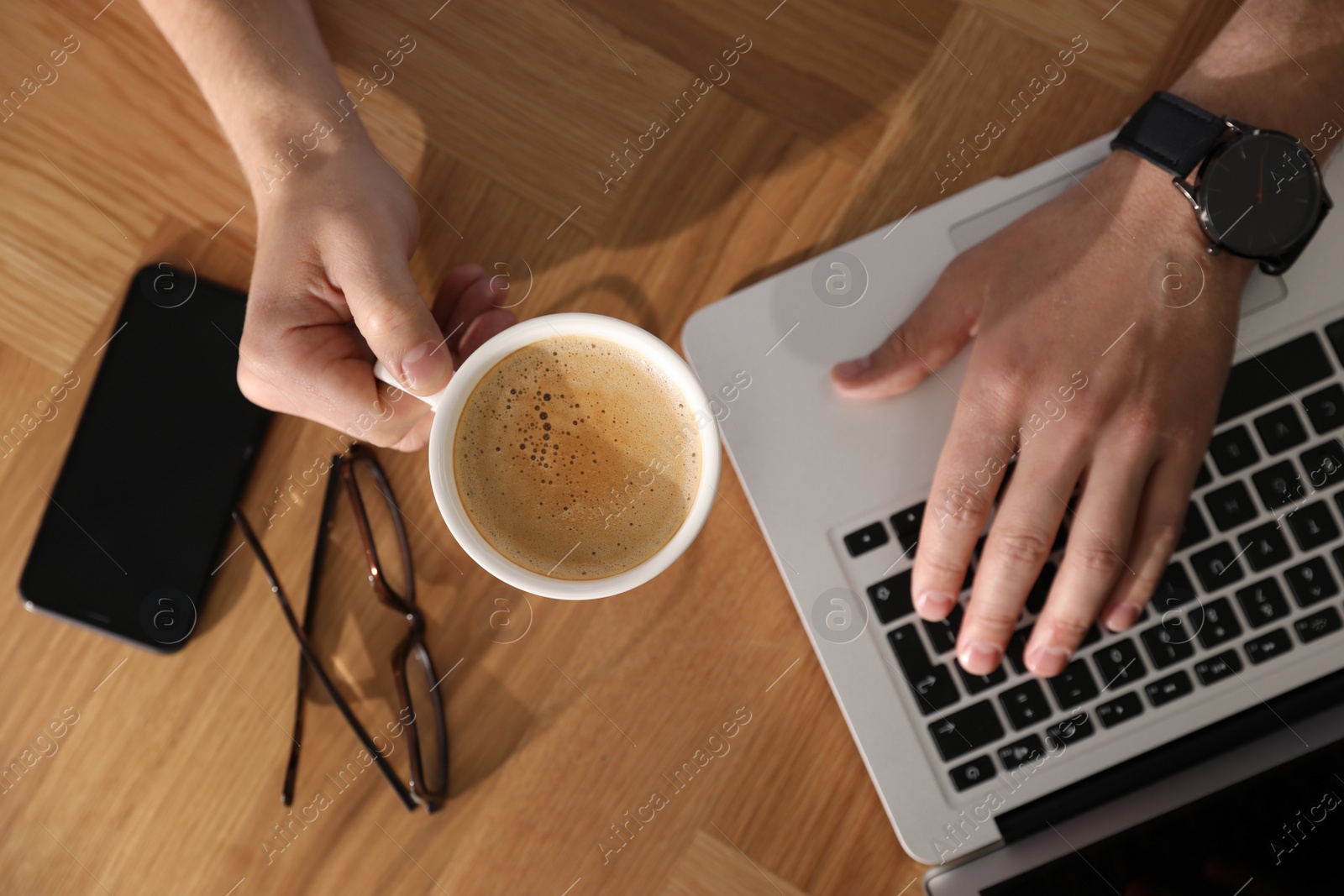 Photo of Man with laptop, cup of coffee and smartphone at wooden table, top view