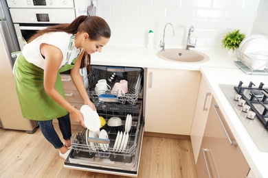 Photo of Beautiful young woman loading dishwasher in kitchen. Cleaning chores