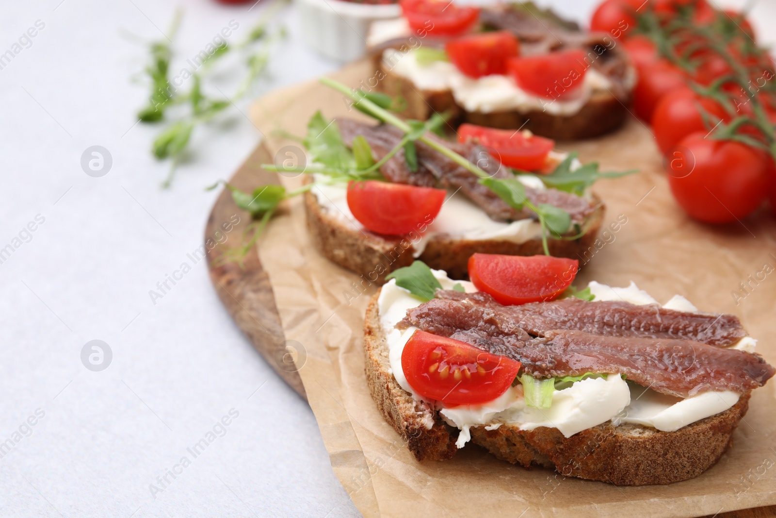 Photo of Delicious bruschettas with anchovies, tomatoes, microgreens and cream cheese on white table, closeup. Space for text