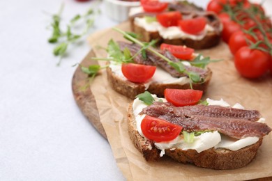 Delicious bruschettas with anchovies, tomatoes, microgreens and cream cheese on white table, closeup. Space for text