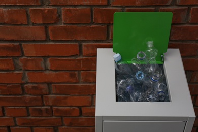 Photo of Many used plastic bottles in metal bin near brick wall, space for text. Recycling problem