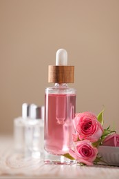 Photo of Bottle of essential rose oil and flowers on white wooden table against beige background
