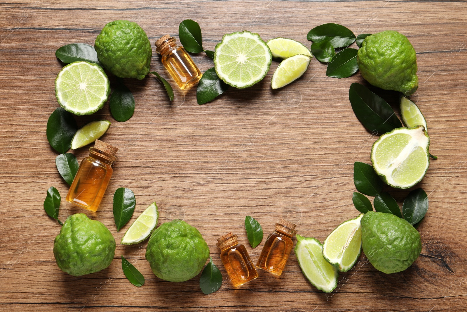 Photo of Frame of glass bottles with bergamot essential oil and fresh fruits on wooden table, flat lay. Space for text