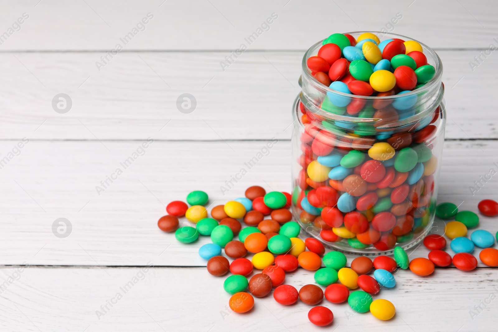 Photo of Tasty colorful candies on white wooden table, space for text