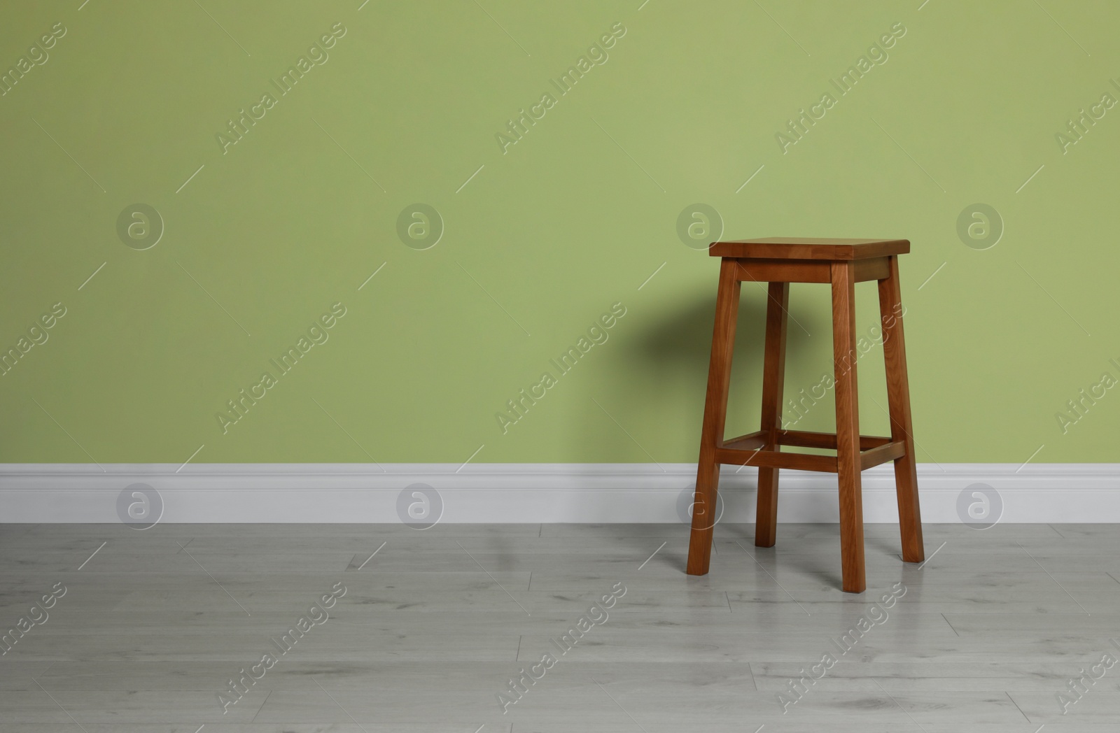 Photo of Stylish wooden stool near light green wall indoors. Space for text