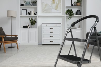 Photo of Metal folding ladder on soft carpet in stylish room
