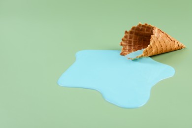 Photo of Melted ice cream and wafer cone on green background. Space for text