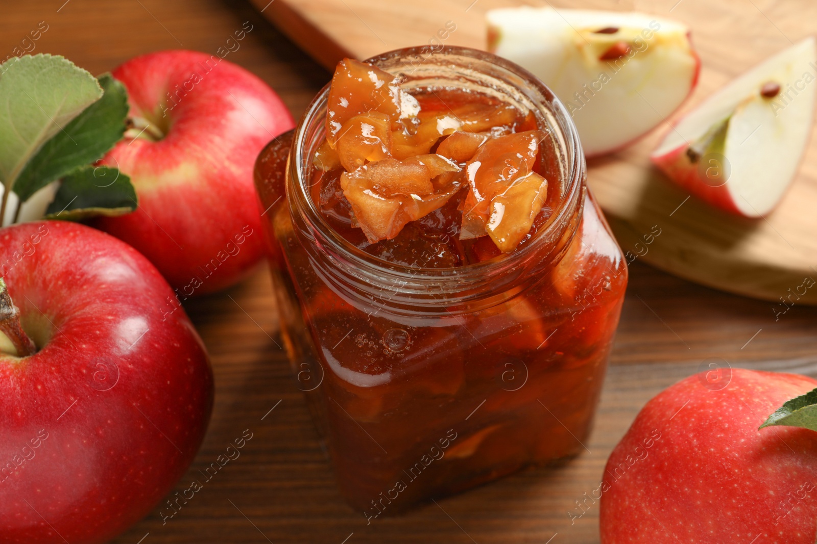 Photo of Tasty apple jam in glass jar and fresh fruits on wooden table