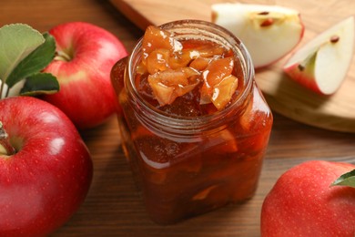 Tasty apple jam in glass jar and fresh fruits on wooden table