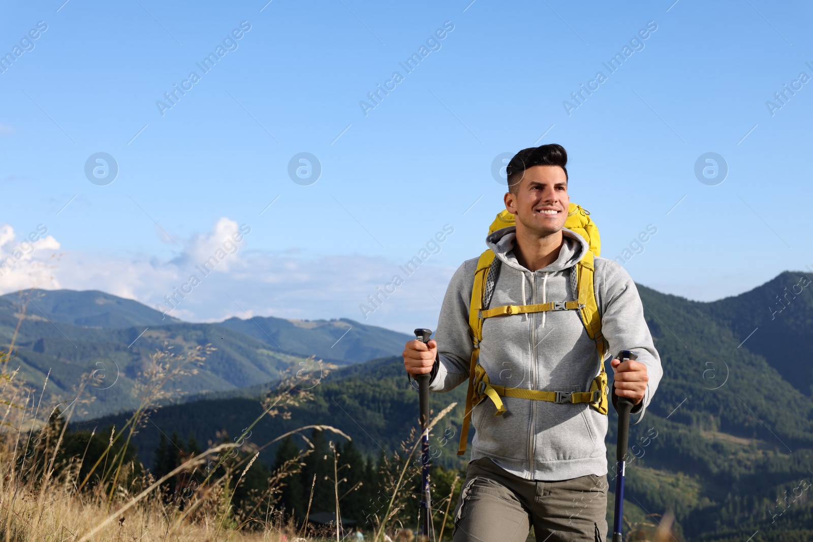 Photo of Tourist with backpack and trekking poles hiking through mountains, space for text