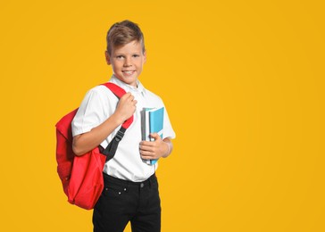 Little boy with backpack and notebooks on yellow background. Back to school