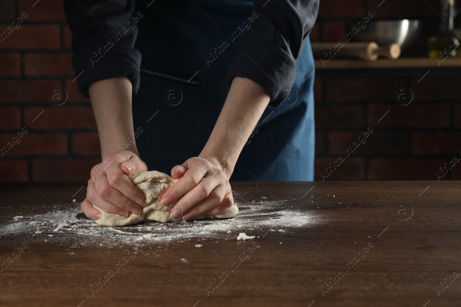 Photo of Making bread. Woman kneading dough at wooden table in kitchen, closeup