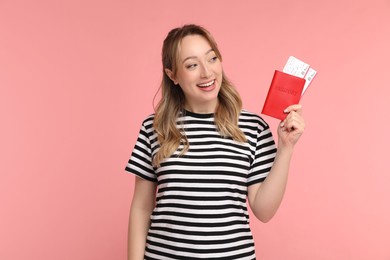 Happy young woman with passport and ticket on pink background