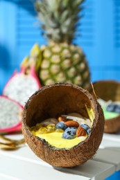 Photo of Tasty smoothie bowl with fresh blueberries and almonds served in coconut shell on white wooden table, closeup