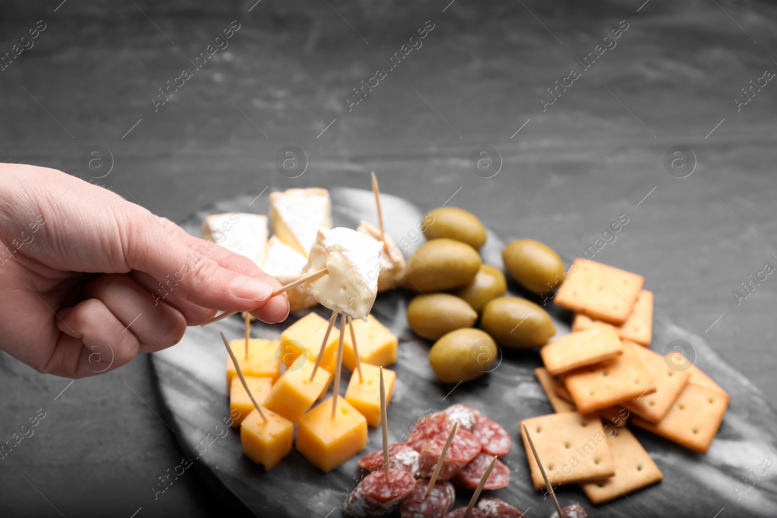 Photo of Woman taking toothpick with piece of cheese at black table, closeup and space for text