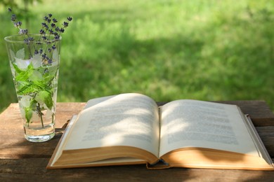 Photo of Open book with flowers in glass on wooden table outdoors