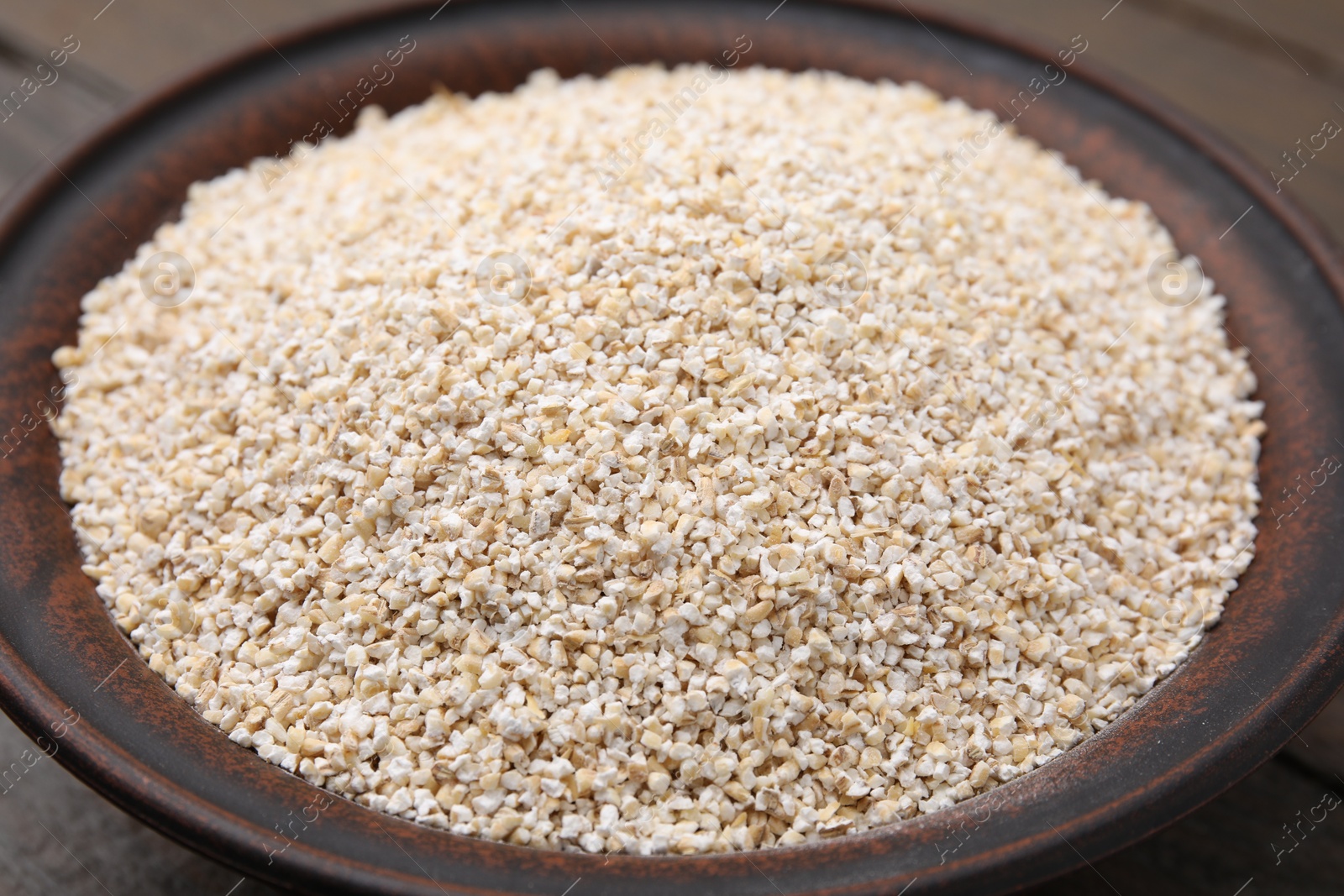 Photo of Raw barley groats in bowl on table, closeup