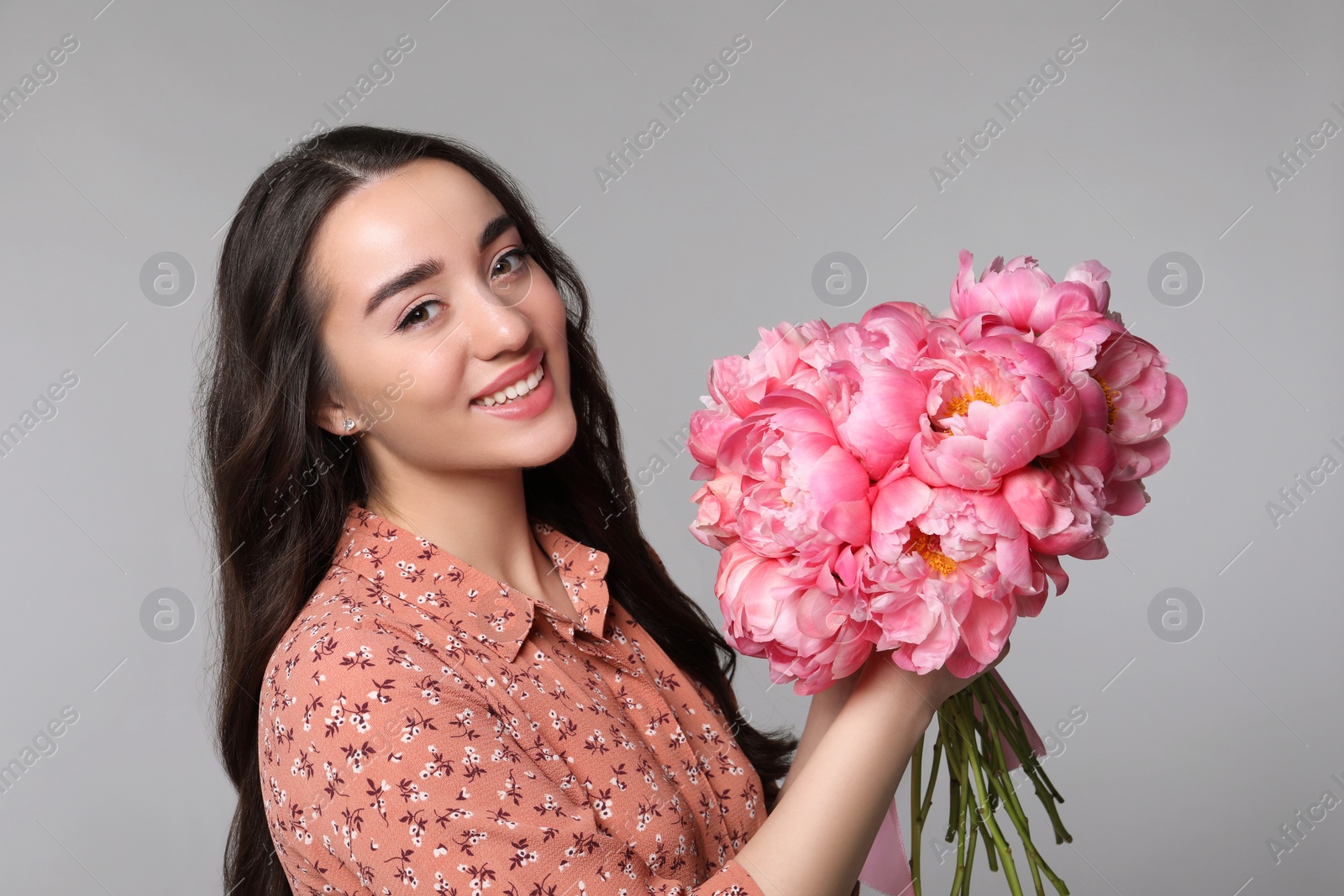 Photo of Beautiful young woman with bouquet of peonies on light grey background