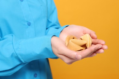 Photo of Young woman holding tasty fortune cookies with predictions on yellow background, closeup